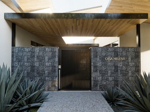 Modern home entrance in Costa Rica featuring stone walls, wood ceiling, and a gate labeled Casa Helena
